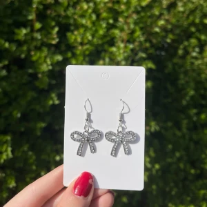 Handgjorda örhängen - rosett med strass (nickelfria) - Ett par handgjorda örhängen i silverfärg med rosettformade hängen dekorerade med små strass-stenar. Krokarna är nickelfria. 🤍 Perfekt att ge som present!!
