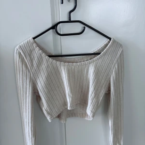 Beige ribbad croppad topp - Säljer en beige croppad topp med långa ärmar och ribbat material. Toppen har en bred, rund halsringning och är perfekt för en trendig och avslappnad stil.