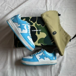 BAPE STA sneakers bapesta blue - Säljer ett par BAPE STA sneakers i blankt blått och vitt skinn med klassisk stjärndesign på sidan. Skorna har vit sula, blå detaljer och snörning med guldfärgade dubbar. Kommer med originalkartong och dustbag. Skorna är i storlek 42,5/43
