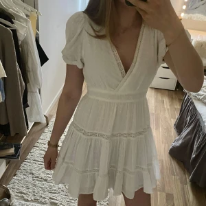 Vit Zara klänning, säljs inte längre - Endast använd 2 gånger! Söt vit kortklänning med omlottliv och v-ringning. Klänningen har korta puffärmar, volang i kjolen och fina spetsdetaljer. Perfekt för sommarens alla tillfällen. Lätt och luftig modell och stretchig☀️💞
