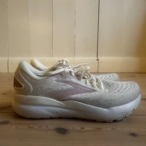Vita och ljusrosa löparskor från Brooks - Säljer ett par snygga löparskor från Brooks i vitt och ljusrosa. Skorna har ventilerande mesh-ovandel, snörning och en tjock, dämpad sula för extra komfort. Perfekta för dig som gillar att springa eller promenera.