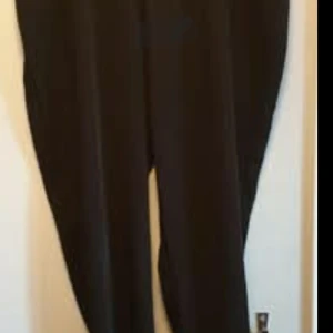 Svarta byxor från Zizzi - Svarta byxor från Zizzi med klassisk rak passform. Perfekta för en stilren look och enkla att matcha med olika toppar. Byxorna har en enkel design utan synliga detaljer och är tillverkade i ett mjukt material.