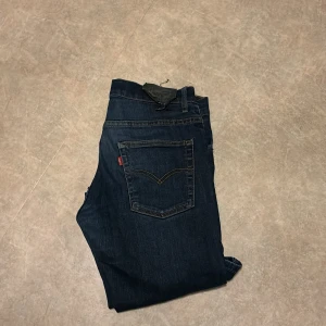 Mörkblå Levis jeans straight fit - Säljer ett par klassiska mörkblå Levis jeans med raka ben och fem fickor. Jeansen har Levis ikoniska röda etikett på bakfickan och snygga kontrastsömmar. Perfekta för dig som gillar tidlös stil och bra passform.