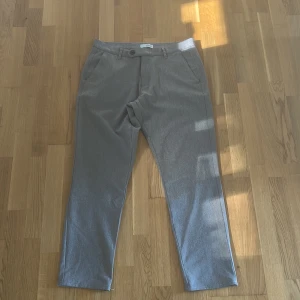Grå chinos  - Snygga grå chinos med klassisk passform. Byxorna har två sidofickor och två bakfickor med knapp. Perfekta för en stilren och enkel look. Materialet känns mjukt och bekvämt.
