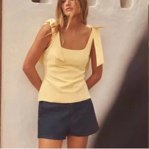 Gul linnetopp med rosettband på axlarna - Snygg gul linnetopp med breda axelband som knyts till rosetter. Den är helt ny med prislappen kvar, glömde returnera den. Kan även tänka mig att byta mot xs❤️