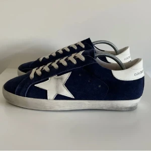 Golden goose skor - Säljer ett par mörkblå sneakers från Golden Goose med vit stjärndetalj på sidan och vita snören. Skorna har vit hälkappa och platt sula. Perfekta för dig som gillar en sportig och trendig stil. Väldigt bra pris. Nästan ny skick box,dust ingår hör av er vid frågor! Byten tas emot!