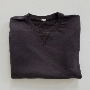 Brun sweatshirt med rund hals - En stilren espresso-brun sweatshirt med rund halsringning och klassisk V-detalj framtill. Tröjan har långa ärmar och ribbade muddar vid ärmslut och nederkant. Perfekt för en avslappnad och enkel look.