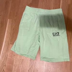 Ljusgröna shorts från EA7 Emporio Armani - Snygga ljusgröna shorts från EA7 Emporio Armani med elastisk midja och sidofickor. Perfekta för sommaren med en avslappnad passform och diskret logga på ena benet.