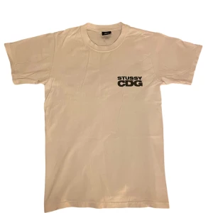 Stussy x CDG t-shirt - Vit t-shirt från Stussy i samarbete med CDG. Tryck med Stussy CDG-logga på bröstet och stort grafiskt tryck på ryggen. Klassisk passform och rund halsringning. Perfekt för dig som gillar streetwear och unika samarbeten. Nypris ligger på runt 1800kr så 650kr är ett väldigt rimligt pris, dessutom så har tröjan knappt blivit använd.