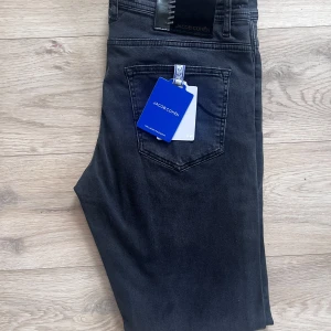 Jacob Cohen BRAND NEW - Snygga svarta jeans från Jacob Cohen med klassisk femficksdesign och diskret logga på bakfickan. Jeansen har normal passform och raka ben, tillverkade i mjukt denimtyg med en stilren look. Perfekta för dig som gillar stilrena och tidlösa jeans.