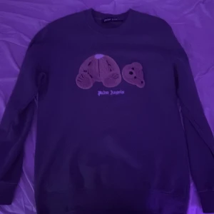 Grå sweatshirt från Palm Angels med nallemotiv - Säljer en grå sweatshirt från Palm Angels med ett unikt nallemotiv på bröstet och logotyp under. Tröjan är i 100% bomull och har långa ärmar. Perfekt för dig som gillar streetwear och vill sticka ut med en cool detalj.