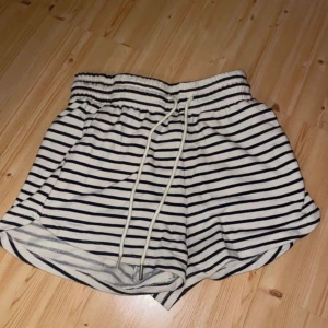 Randiga shorts med dragsko - Snygga shorts med svartvita ränder och elastisk midja med vit snörning. Perfekta för sommaren och har en avslappnad passform. Tillverkade i mjukt bomullsmaterial för extra komfort.