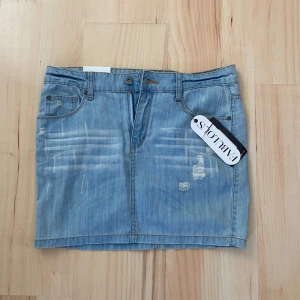 Ljusblå jeanskjol - Ljusblå jeanskjol med slitna detaljer och klassisk femficksdesign. Kjolen har bälteshällor och knappstängning framtill. Perfekt för en avslappnad och trendig look. Kom med bud!