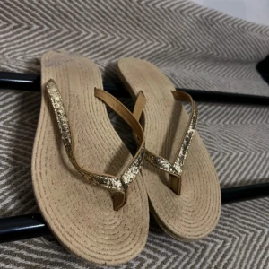 Beige sandaler med glittriga remmar - Säljer ett par snygga sandaler i beige med glittriga guldiga remmar. Perfekta för varma dagar och ger en trendig touch till din outfit. Lätta att bära och passar till många olika stilar.