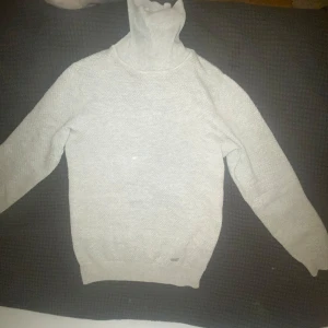 Ljusgrå stickad polotröja - Säljer en ljusgrå stickad polotröja med lång ärm. Tröjan har en hög polokrage och är perfekt för kyligare dagar. Enkel och stilren design som passar till mycket.