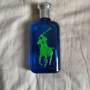 Ralph Lauren Polo Blue parfym - Fräsch herrparfym från Ralph Lauren i en stilren blå glasflaska med silverfärgad kork. Flaskan har den klassiska gröna Polo-loggan med en polospelare. Perfekt för dig som gillar sportiga och fräscha dofter. Låda kommer med också.