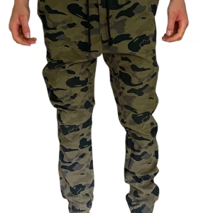 Cargobyxor i camouflage med dragsko - Säljer ett par gröna cargobyxor med camouflage-mönster och svarta dragsnören i midjan. Byxorna har resår i midjan och smal passform vid anklarna. Perfekta för en avslappnad streetstil. Det finns en liten fläck på framsidan men den stör intr utseendet —> bild 5