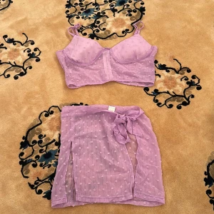 Ljuslila mesh topp och kjol-set - Säljer ett ljuslila set med croppad mesh topp och matchande kjol. Toppen har smala axelband, lätt vadderade kupor och dragkedja bak. Kjolen är transparent med knyt i midjan och slits. Båda delar har små prickiga detaljer.