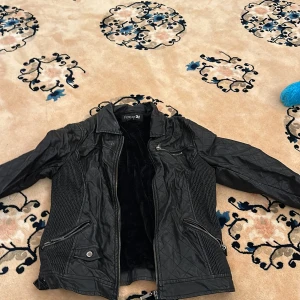 Svart quiltad skinnjacka med fuskpälsfoder - Säljer en svart skinnjacka från Forever 21 med quiltade detaljer och mjukt fuskpälsfoder. Jackan har dragkedjor framtill och på fickorna samt en klassisk krage. Perfekt för kyligare dagar.