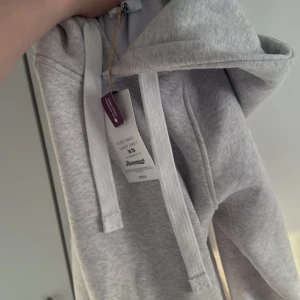 Ljusgrå hoodie från Russemerch - Säljer en ljusgrå hoodie från Russemerch i mjuk bomullsblandning. Tröjan har huva med magficka och ribbade muddar vid ärmslut och nederkant. Perfekt för en avslappnad stil.