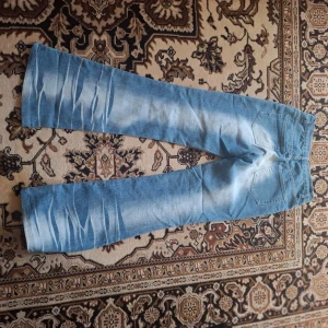 Ljusblå bootcut jeans - Säljer ett par ljusblå jeans med bootcut passform och tydliga slitningar. Jeansen har klassiska bakfickor och är tillverkade i denim. Perfekta för en avslappnad och trendig look.