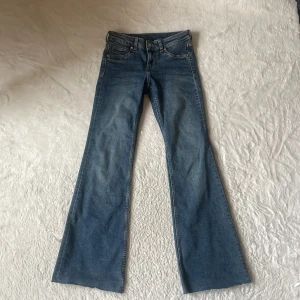 Blå bootcut jeans från H&M - Säljer ett par klassiska blå bootcut jeans från H&M med fem fickor och normalhög midja. Jeansen har en snygg tvätt och stängs med knapp och dragkedja. Perfekta för dig som gillar en tidlös jeanslook.