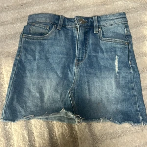 Jeanskjol från LAB Industries - Säljer en klassisk blå jeanskjol från LAB Industries med rå kant nertill och slitningar framtill. Kjolen har fem fickor. Använd få tal gånger.