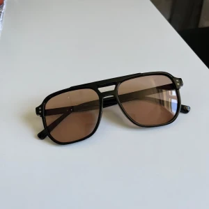 Svarta solglasögon med bruna glas - Snygga svarta solglasögon med bruna glas och klassisk pilotform. Bågarna är i plast och har en stilren design med dubbla bryggor. Perfekta för att lyfta din look under soliga dagar.