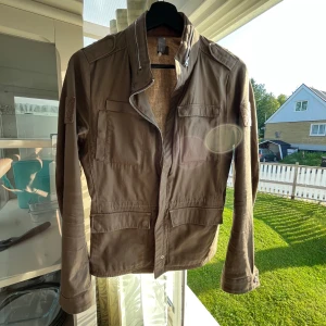 Brun vindjacka från G-Star RAW - Snygg brun vindjacka från G-Star RAW med coola detaljer som axelpartier, flera fickor och dragkedja framtill. Jackan har en rak passform och är tillverkad i bomull, perfekt för dig som gillar streetstyle och vill ha en stilren look.