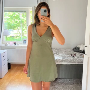 Olivgrön satin klänning - Super fin olivgrön satin klänning från Bikbok som använts 2 gånger💚tyvärr har den deo-fläckar (se bild 2 & 3) men tror de går bort i tvättmaskinen💚hör av dig vid frågor!!