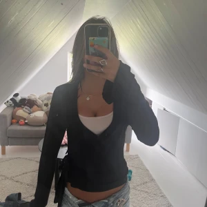 Svart omlottkofta från Gina Tricot - Svart omlottkofta från Gina Tricot i storlek S. Koftan har lång ärm, v-ringning och knyt i sidan för en snygg passform. Perfekt att styla med jeans eller kjol för en trendig look.
