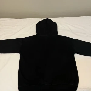 Svart hoodie från Eternity - En klassisk svart hoodie från Eternity med huva och känguruficka framtill. Tröjan har lång ärm och ribbade muddar vid ärmslut och nederkant. Perfekt för en chill och avslappnad stil.