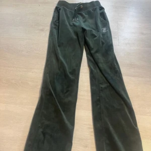 Juicy Couture gröna  - Gröna velourbyxor från Juicy Couture med breda ben och glittrande strasstext på baksidan. Byxorna har snörning i midjan och en liten strasslogga framtill. Använda 2 gånger 