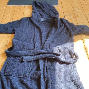 Mörkblå frottérock från Kappahl - Mysig mörkblå frottérock från Kappahl med huva och knytskärp i midjan. Perfekt att slänga på sig efter duschen eller när du chillar hemma. Har två stora fickor framtill och är tillverkad i mjuk frotté som känns skön mot huden. Har aldrig använt.