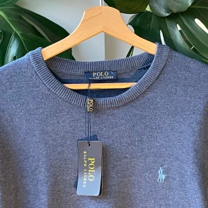 Blå tröja från Polo Ralph Lauren - Snygg blå tröja från Polo Ralph Lauren med rund halsringning och broderad logga på bröstet. Tröjan har ribbade muddar vid hals, ärmslut och nederkant. Perfekt för dig som gillar klassisk och stilren design.