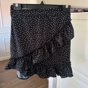 Svart prickig volangkjol - Supersöt svart kortkjol med vita prickar och volangdetaljer.