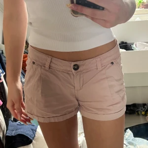 Ljusrosa shorts från Blind Date - Snygga ljusrosa shorts från Blind Date med uppvikta benslut, bälteshällor och knäppning fram. Shortsen har fickor både fram och bak med knappdetaljer. Perfekta för varma dagar och en chill look.