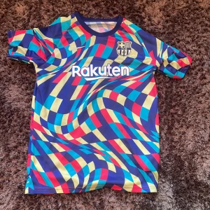 FC Barcelona Nike Dri-FIT träningströja - Säljer en FC Barcelona träningströja från Nike med Dri-FIT-material. Tröjan har ett galet färgstarkt, psykedeliskt mönster i blått, rött, gult och grönt. Kortärmad modell med klubbmärke, Rakuten och Beko-loggor. Perfekt för dig som vill sticka ut på planen. Sitter som small.