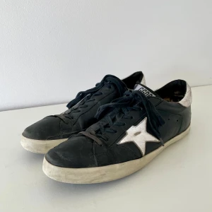 Golden goose skor - Golden goose sneakers i svart skinn med vit stjärna. Klassisk låg model med snörning och platt sula. Mycket använda och slitna med mycket kvar att ge. Sömmen mellan sulan och överdelen har lossnat lite vid sidan. Hål i hälarna på båda skorna. 5600 kr nypris. Order bekräftelse från vestiare finns så de är äkta. Hör av dig för funderingar.