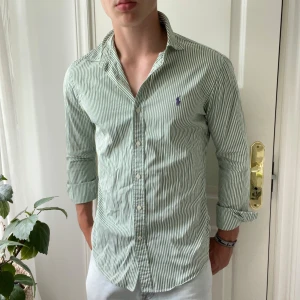 Ralph Lauren grön randig skjorta - Skick 7/10, svett fläckar under båda armar och en pytte pytte liten fläck vid kragen som jag kan skicka bild på, modellen är 180 cm,75 kg och bär M slim fit. 