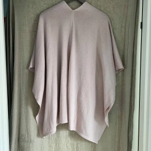 Ljusrosa poncho - Supermjuk och flowy ljusrosa poncho med omlott-look och v-ringning. Den är stickad,  i viskos  och har en avslappnad  passform. Perfekt att slänga över en topp för en chill och stilren vibe.