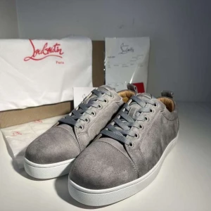 Grå mockasneakers från Louboutin - Snygga grå sneakers från Christian Louboutin i mjuk mocka med klassisk röd sula och vita kanter. Skorna har rund tå, platt sula och grå snörning. Insidan är fodrad i beige skinn för extra komfort. Perfekta för dig som vill ha en clean och exklusiv look.