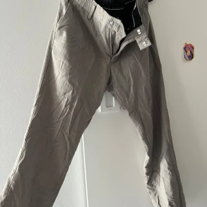 Beige kostymbyxor i linneblandning - Snygga beige kostymbyxor i storlek 46 med klassisk passform. Byxorna har två bakfickor med knapp, bälteshällor och stängs med hake och dragkedja. Perfekta för en clean och stilren look, tillverkade i ett lätt material som känns luftigt. Kostar ny 1200:-. Tiger of Sweden