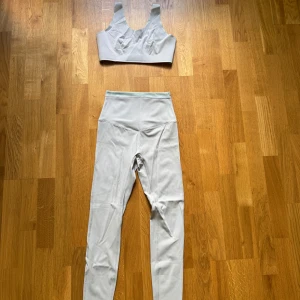 Vit sportig topp tillsammans med matchande tights  - Snygg vit topp med breda axelband och sportig design samt matchande tights till. Perfekt för träning och aktiva dagar, tillverkad i stretchigt syntetmaterial som andas. 