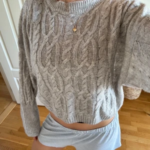 Grå stickad tröja från NA-KD - Supermysig grå stickad tröja från NA-KD med grovt kabelstickat mönster. Tröjan är croppad med ribbade muddar och har lång ärm. Perfekt till höst och vinter för en chill och snygg look.