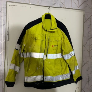 Gul Tranemo varseljacka med reflex - Varseljacka från Tranemo Workwear i gul och svart med breda reflexband runt bröst, armar och rygg. Jackan har dragkedja framtill, hög krage och flera fickor. Materialmix av bomull och syntet, perfekt för dig som vill sticka ut på jobbet.