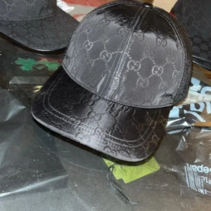 Svart keps från Gucci med GG-mönster DUST BAG OCH LÅDA INGÅR! - Snygg svart keps från Gucci med klassiskt GG-monogram över hela framsidan. Kepsen har mesh på baksidan för extra ventilation och justerbar snapback. Tillverkad i polyester och har en stilren, glansig finish. Perfekt för dig som vill ha en exklusiv streetstyle-look.
