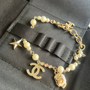 Chanell armband med pärlor och berlocker - Superfint armband m i guldton med vita pärlor och gnistrande stenar. Armbandet har berlocker som stjärna, CC-logga och en liten ansiktsberlock. Perfekt statement piece för dig som vill sticka ut med lyxig vibe.