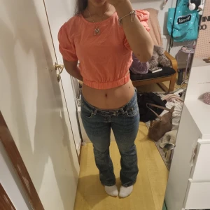 Korallrosa croppad topp med puffärm - Superfin korallrosa croppad topp med korta puffärmar och resår i midjan. Toppen har en snygg öppen detalj i sidan som ger en cool twist. Perfekt för dig som gillar färg och vill sticka ut lite extra. Passar till både jeans och kjol!