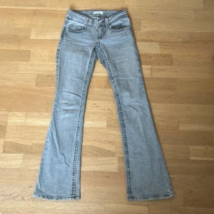 Grå bootcut jeans från Gina Tricot - Snygga grå jeans från Gina Tricot. De har bootcut-ben, låg midja och coola bakfickor med lock och knapp. Jeansen är i klassisk denim med en ljusgrå tvätt och passar perfekt till sneakers!